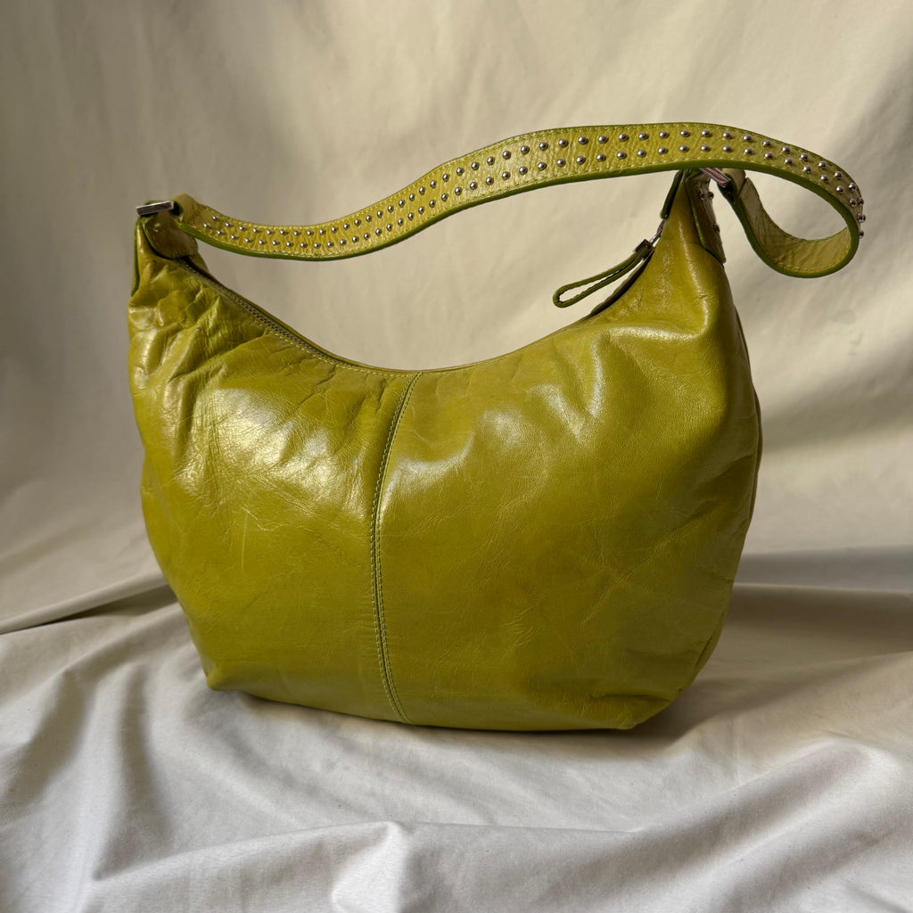 A yellow-green leather hobo shoulder bag with a matching studded strap, displayed on a draped white fabric background.