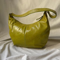 A yellow-green leather hobo shoulder bag with a matching studded strap, displayed on a draped white fabric background.